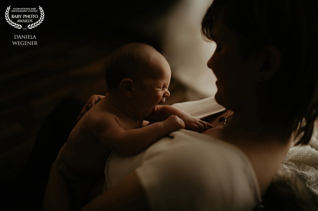 Foto mit Auszeichnung von einer Mutter mit Neugeborenem, welches gähnt, auf der Brust im Gegenlicht
