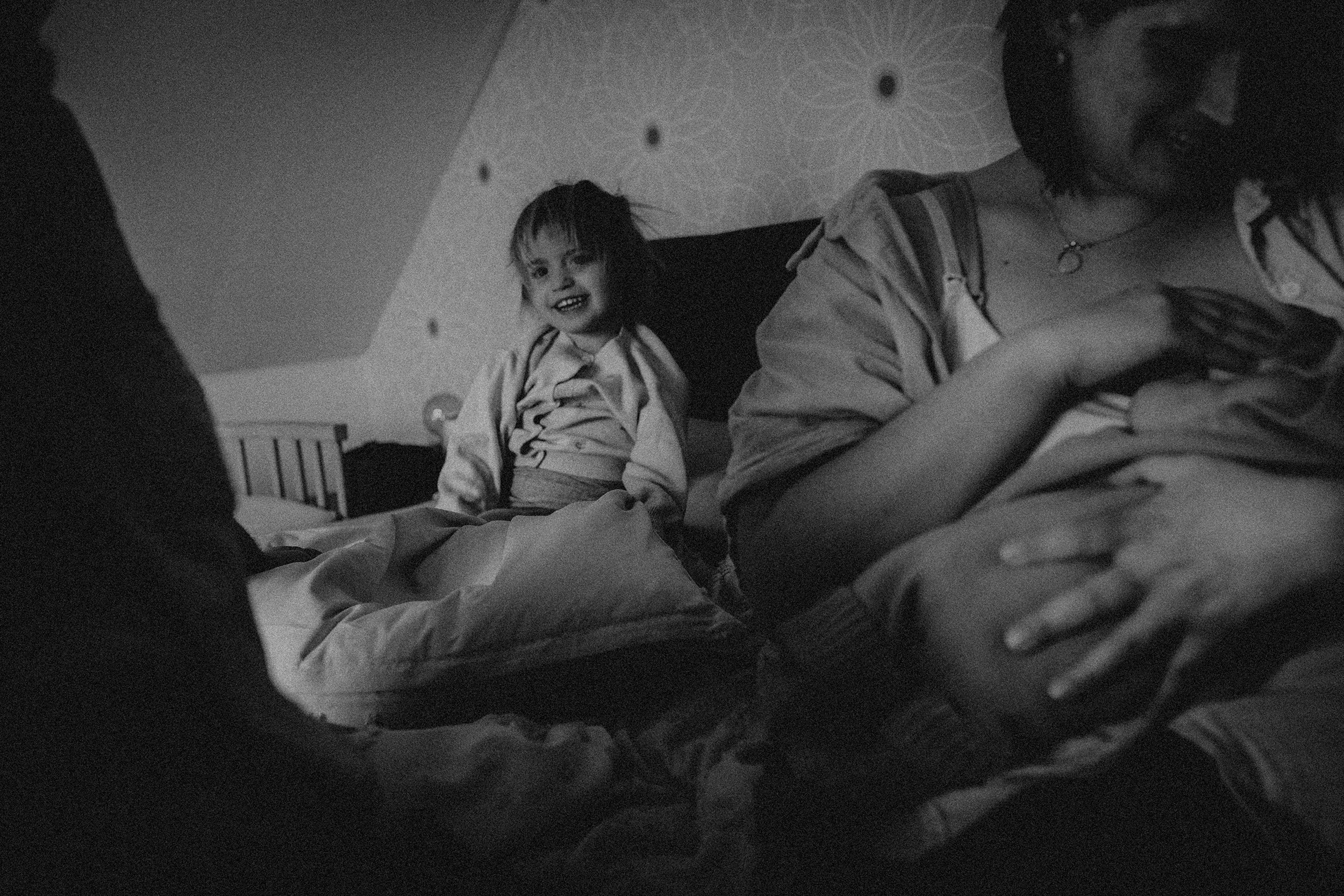 schwarz-weiß Aufnahme eines Kindes mit zerzausten haaren, unscharf im Vordergrund die stillende Mama und Geschwisterkind